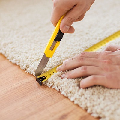 repair, building and home concept - close up of male hands cutting carpet with blade
